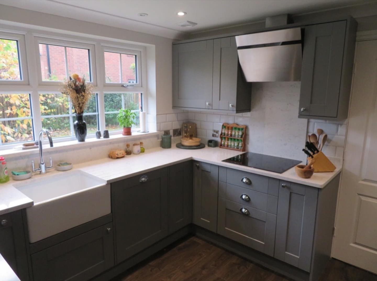 Grey Shaker-style kitchen with a Belfast sink, white worktops, metro tile splashback and angled cooker hood