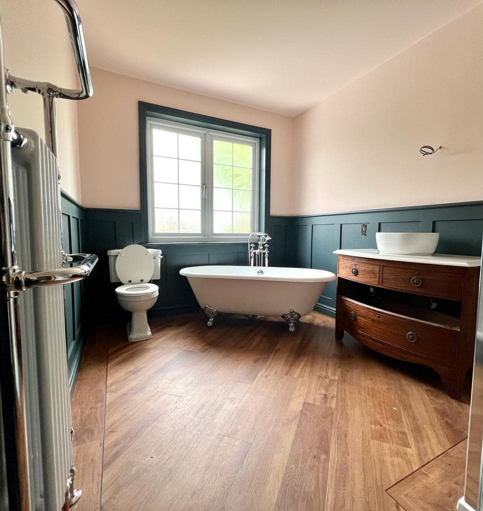 Traditional bathroom with a roll-top bath, dark green panelling, timber vanity and wood-effect floor