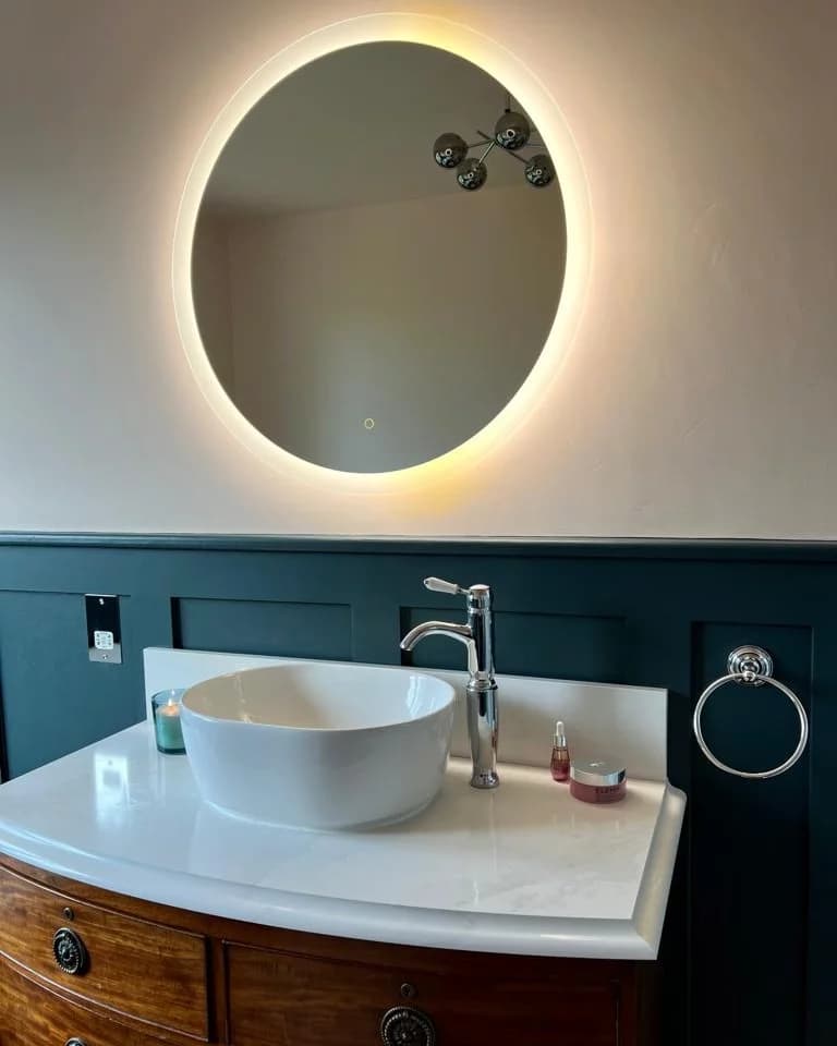 Bathroom vanity with a white vessel basin, chrome tap, dark green wall panelling and a round backlit mirror