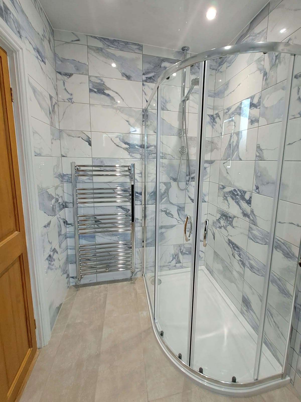 Shower room with marble-effect tiles, an offset quadrant shower enclosure and a chrome heated towel rail