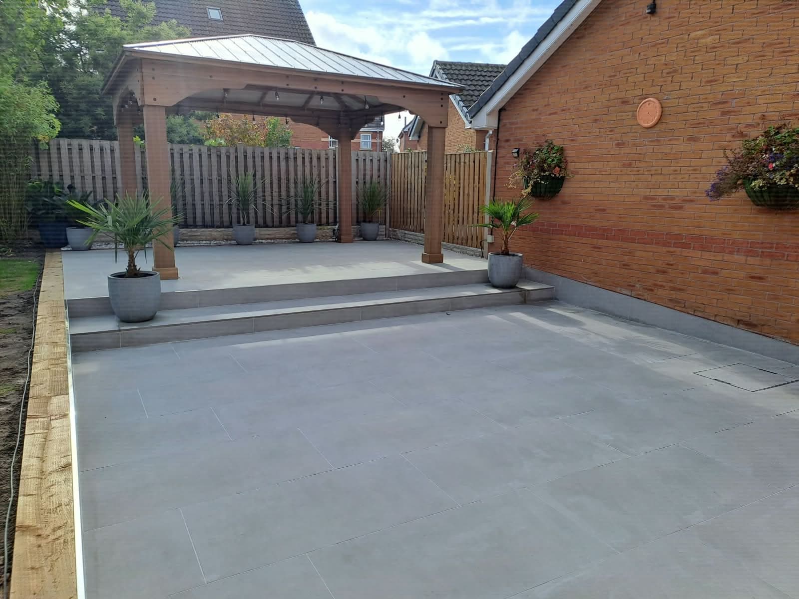 Large-format grey porcelain patio with a raised terrace, steps and a timber gazebo